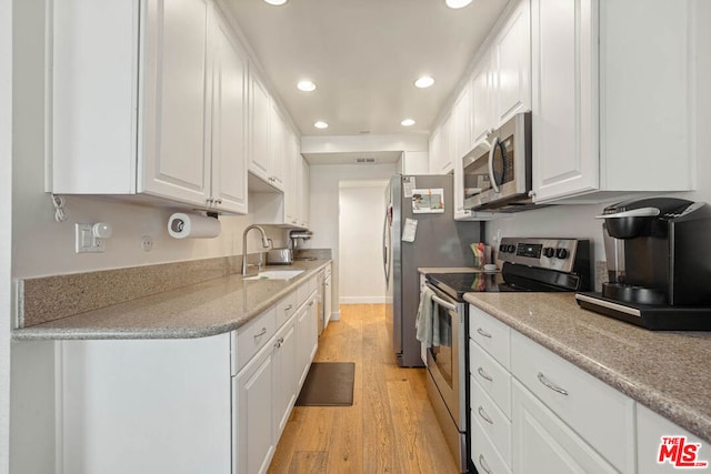 kitchen with appliances with stainless steel finishes, sink, white cabinets, and light hardwood / wood-style floors