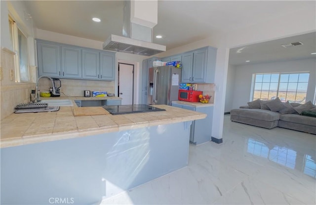 kitchen with exhaust hood, high end refrigerator, tile counters, and kitchen peninsula