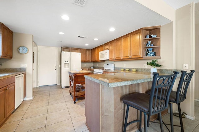 kitchen featuring light tile patterned flooring, a kitchen bar, light stone counters, kitchen peninsula, and white appliances