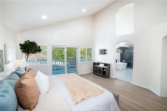 bedroom featuring ensuite bathroom, light hardwood / wood-style floors, high vaulted ceiling, and access to outside