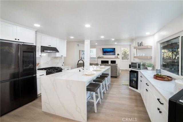 kitchen with a breakfast bar area, appliances with stainless steel finishes, a kitchen island with sink, wine cooler, and white cabinets