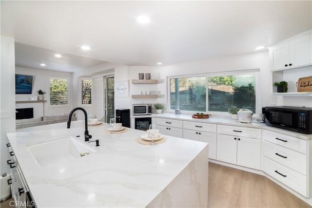 kitchen featuring light stone counters, a healthy amount of sunlight, sink, and white cabinets