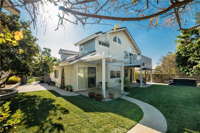 rear view of property featuring a hot tub, a pergola, a lawn, and a patio area