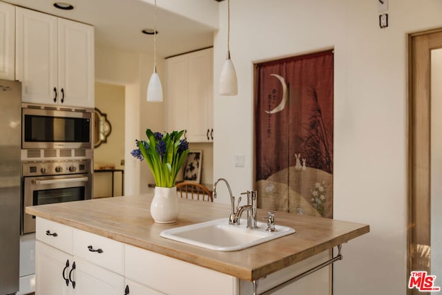 kitchen featuring sink, stainless steel appliances, decorative light fixtures, and butcher block countertops