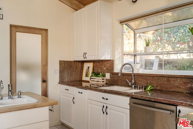 kitchen featuring white cabinetry, sink, stainless steel dishwasher, and dark stone counters