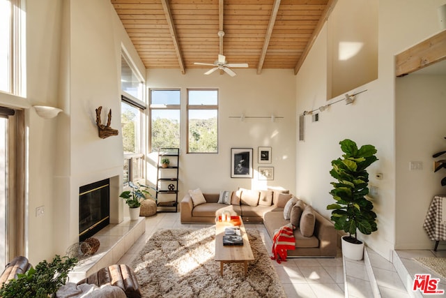 living room featuring light tile patterned floors, wood ceiling, a towering ceiling, a fireplace, and beamed ceiling