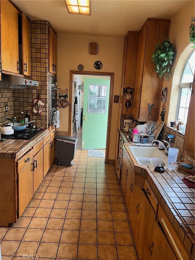 kitchen featuring sink, tile countertops, light tile patterned floors, black gas cooktop, and decorative backsplash