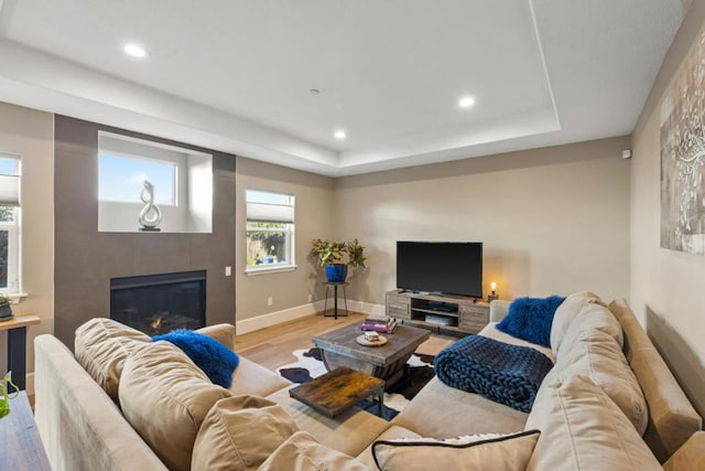 living room with a tiled fireplace, light wood-type flooring, and a tray ceiling