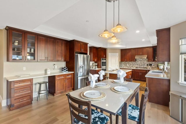 kitchen featuring appliances with stainless steel finishes, light hardwood / wood-style flooring, pendant lighting, and a tray ceiling