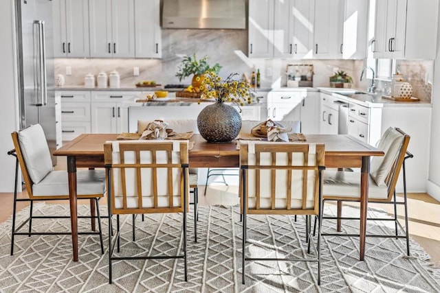 kitchen featuring wall chimney range hood, sink, stainless steel appliances, white cabinets, and decorative backsplash