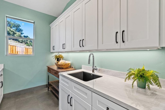 kitchen featuring light tile patterned floors, light stone countertops, sink, and white cabinets