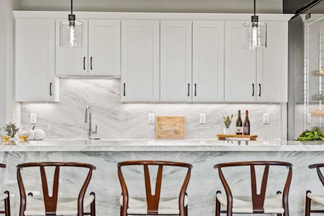 bar featuring light stone counters, hanging light fixtures, and white cabinets