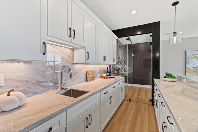 kitchen with pendant lighting, sink, backsplash, white cabinets, and light hardwood / wood-style floors