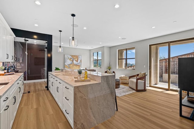 kitchen featuring hanging light fixtures, white cabinets, and light stone counters