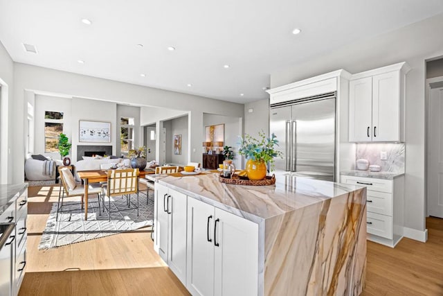 kitchen featuring white cabinetry, stainless steel built in fridge, light stone counters, and light wood-type flooring