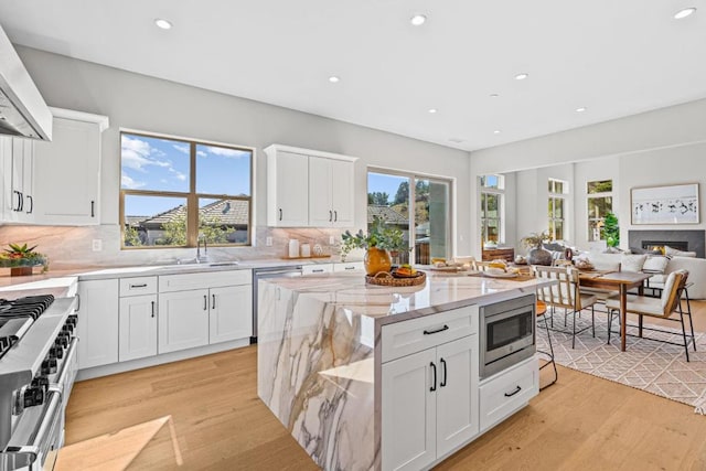 kitchen with sink, stainless steel appliances, light stone countertops, white cabinets, and wall chimney exhaust hood