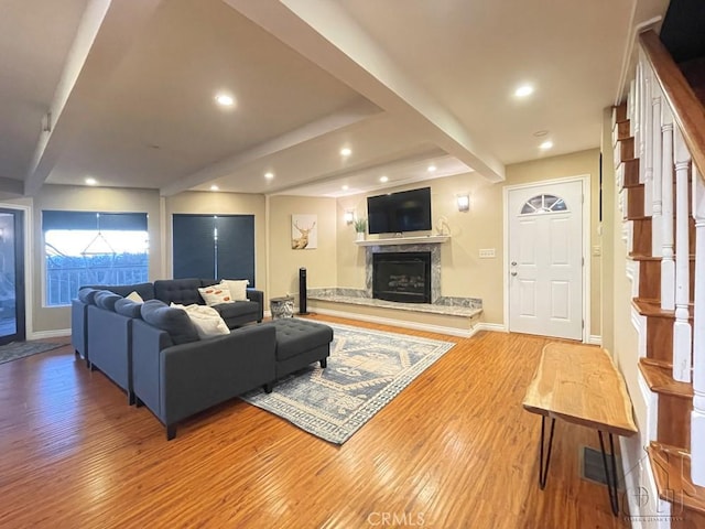 living room with beam ceiling, a premium fireplace, and light hardwood / wood-style floors