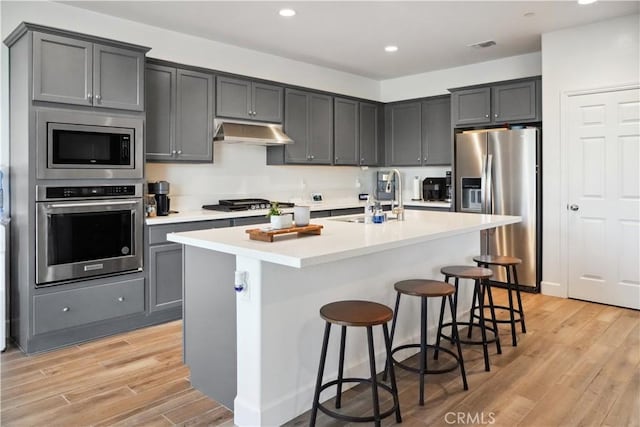 kitchen featuring gray cabinets, appliances with stainless steel finishes, a kitchen island with sink, and a breakfast bar area