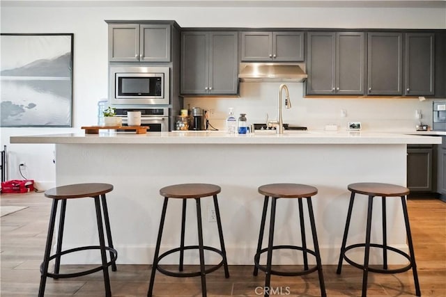 kitchen featuring gray cabinets, appliances with stainless steel finishes, an island with sink, a breakfast bar area, and light hardwood / wood-style floors