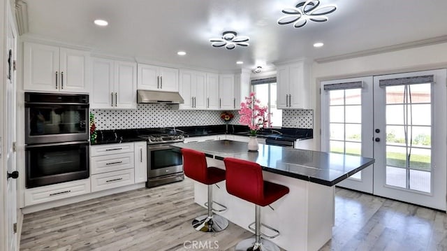 kitchen featuring stainless steel gas range, double oven, a center island, white cabinets, and french doors