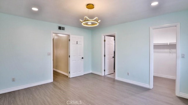 unfurnished bedroom with a notable chandelier, a walk in closet, a closet, and light wood-type flooring