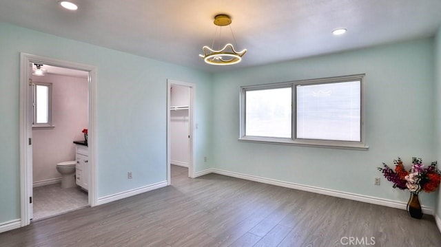 bedroom featuring an inviting chandelier, hardwood / wood-style floors, ensuite bath, and a walk in closet