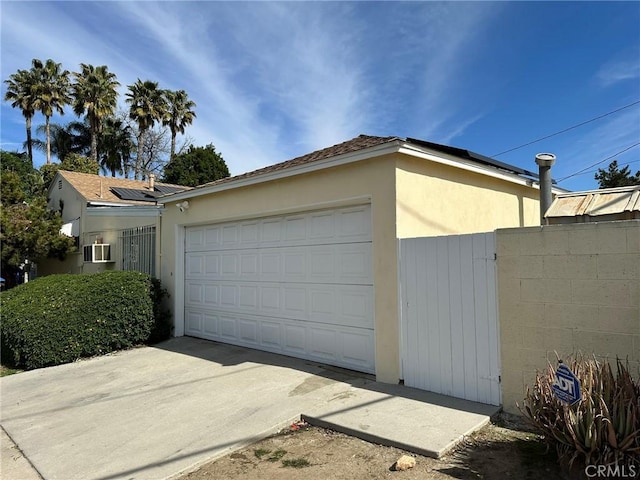 garage featuring driveway, roof mounted solar panels, and fence