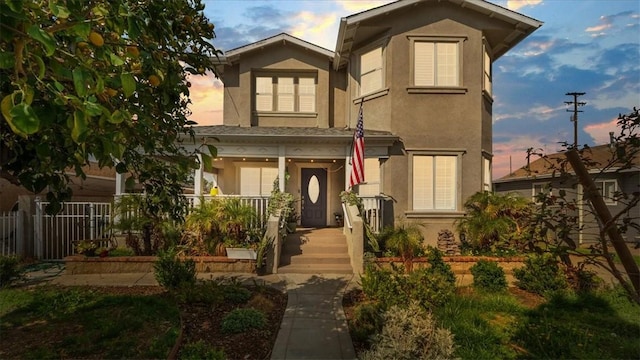view of front facade with a porch, stucco siding, and fence