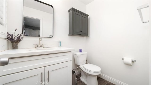 bathroom with toilet, wood finished floors, vanity, and baseboards