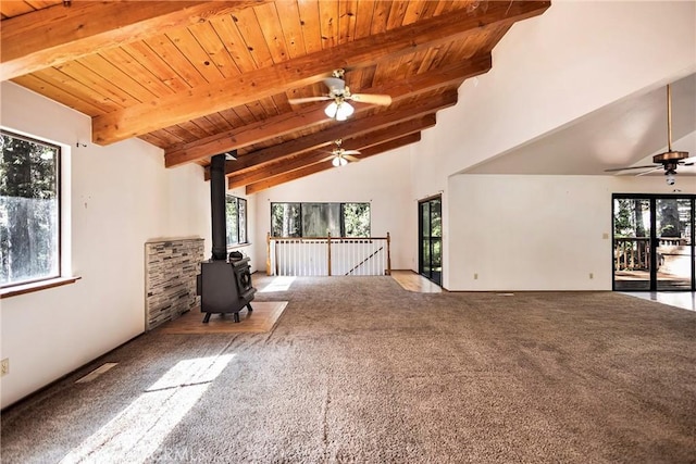 unfurnished living room featuring high vaulted ceiling, carpet floors, a wood stove, ceiling fan, and beam ceiling