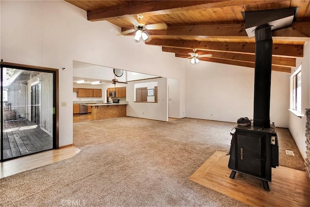 carpeted living room with wood ceiling, lofted ceiling with beams, ceiling fan, and a wood stove