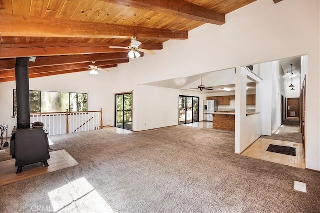 interior space with high vaulted ceiling, light colored carpet, wooden ceiling, and a wood stove