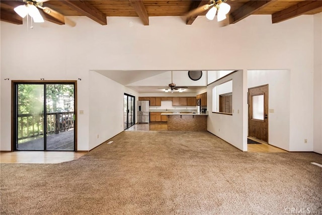 unfurnished living room with beam ceiling, ceiling fan, light colored carpet, and wood ceiling