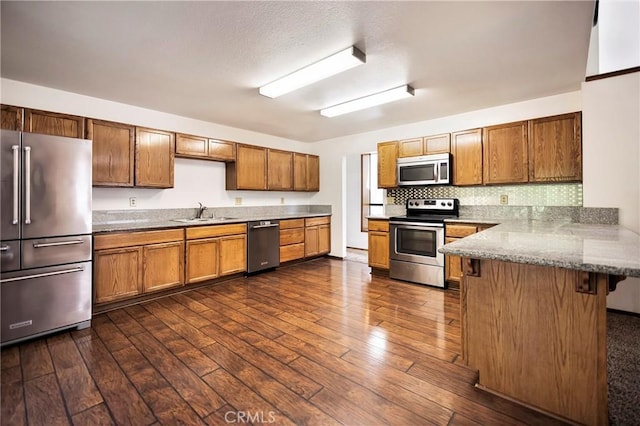 kitchen with sink, stainless steel appliances, dark hardwood / wood-style floors, a kitchen bar, and kitchen peninsula