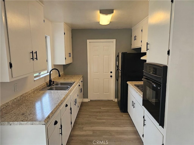 kitchen with white cabinetry, sink, light hardwood / wood-style floors, and black appliances