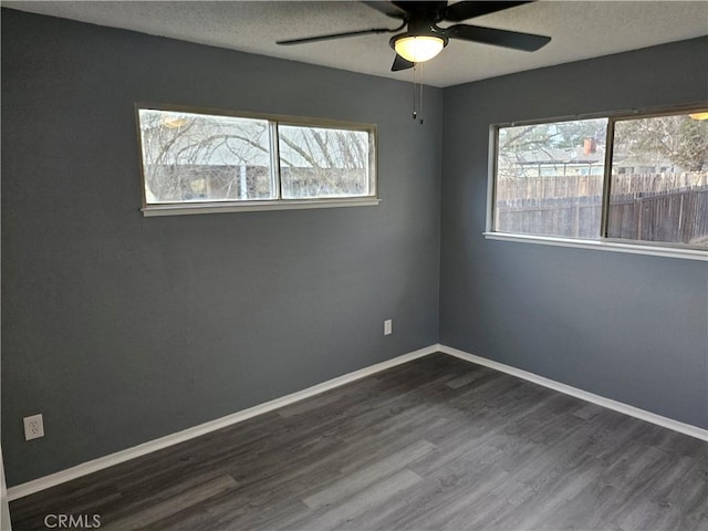 empty room featuring ceiling fan, a healthy amount of sunlight, and dark hardwood / wood-style floors