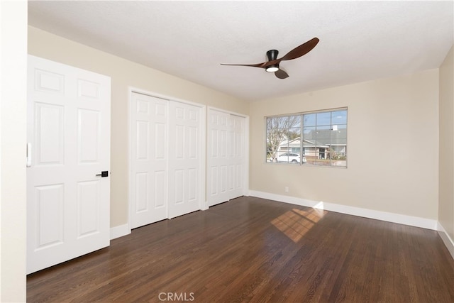 unfurnished bedroom featuring multiple closets, dark hardwood / wood-style floors, and ceiling fan