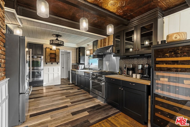 kitchen with wood counters, wood-type flooring, beverage cooler, hanging light fixtures, and stainless steel appliances