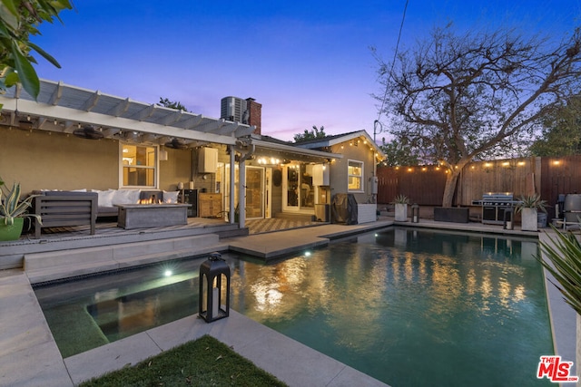 pool at dusk featuring a patio area, grilling area, central AC unit, a pergola, and an outdoor living space with a fire pit