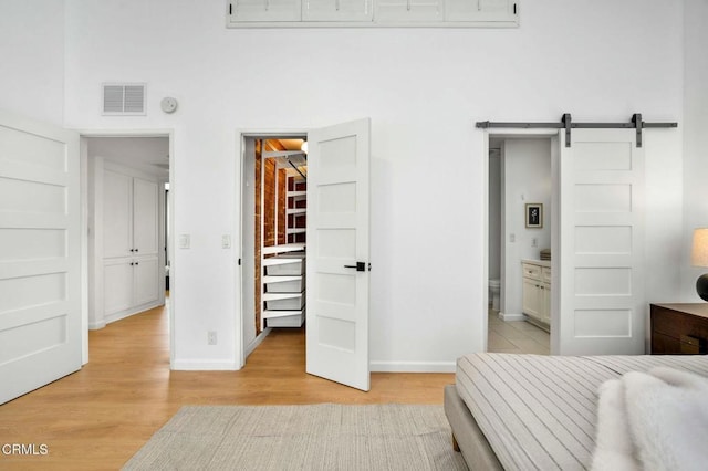 bedroom featuring light wood-type flooring, a walk in closet, a barn door, and ensuite bathroom