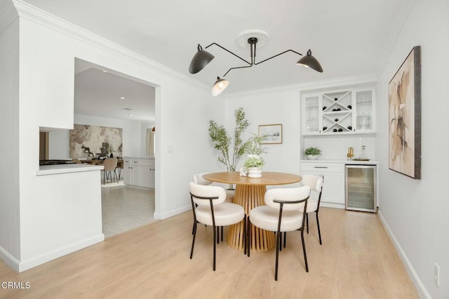 dining space with wine cooler, ornamental molding, bar area, and light hardwood / wood-style floors