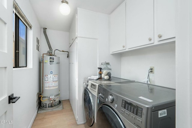 washroom featuring cabinets, washing machine and clothes dryer, light hardwood / wood-style floors, and gas water heater