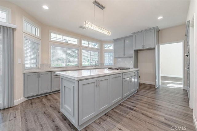 kitchen featuring a kitchen island, tasteful backsplash, gray cabinetry, hanging light fixtures, and light hardwood / wood-style floors