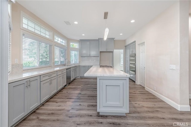 kitchen with gray cabinets, a kitchen island, appliances with stainless steel finishes, sink, and hanging light fixtures