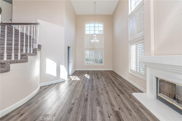 unfurnished living room featuring hardwood / wood-style floors, a towering ceiling, and a notable chandelier