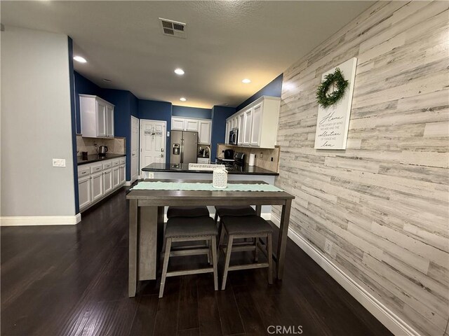 kitchen with white cabinetry, stainless steel appliances, wooden walls, and dark hardwood / wood-style flooring