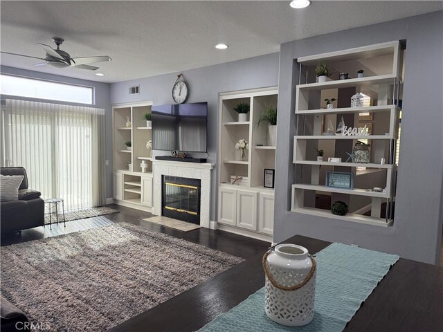 living room with ceiling fan, dark hardwood / wood-style floors, a textured ceiling, and built in shelves