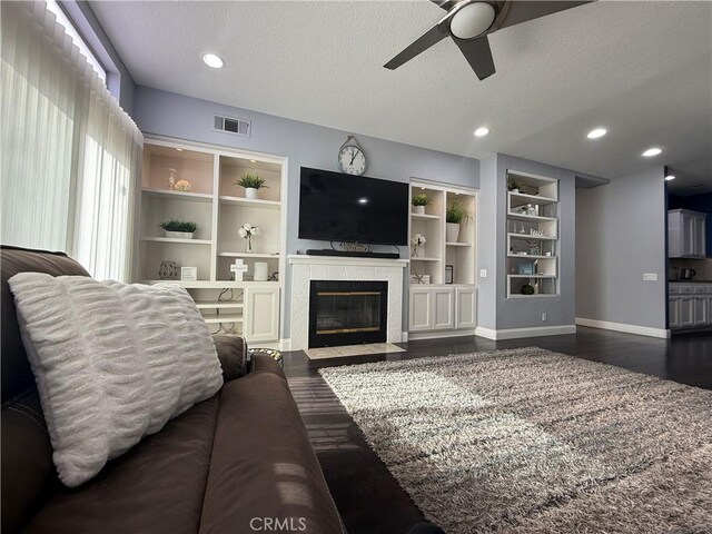 living room with dark wood-type flooring, built in features, ceiling fan, a fireplace, and a textured ceiling