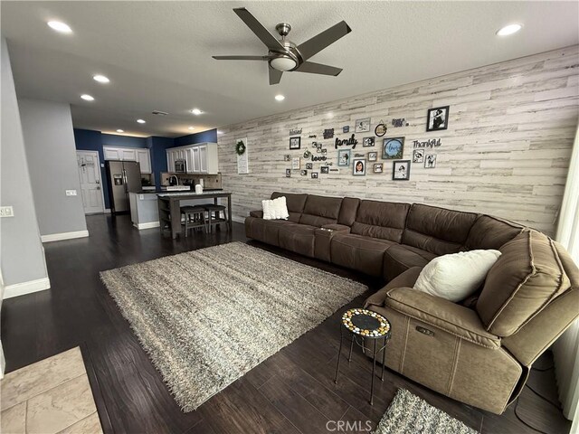 living room with dark wood-type flooring, ceiling fan, and wooden walls