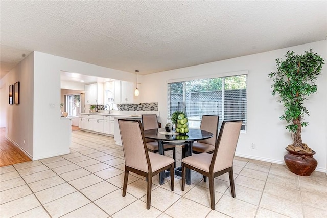 dining area featuring light tile patterned flooring, a textured ceiling, and baseboards